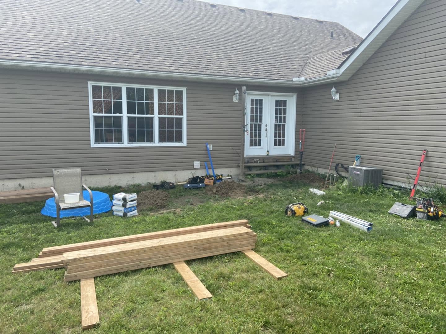 Backyard before renovation with lumber and tools on the grass